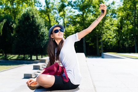 Young Asian woman making selfie pictures outdoors in the park in a sunny dayの写真素材