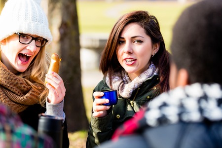 Young female friends talking while drinking a hot beverage outdoors in a winter dayの写真素材