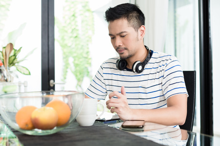 Indonesian man drinking coffee at breakfast listening to music and surfing the internetの写真素材