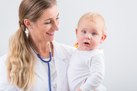 Portrait of a dedicated female physician and pediatric care specialist, smiling while holding a cute and healthy baby girl at the hospital or in a medical healthcare centerの写真素材
