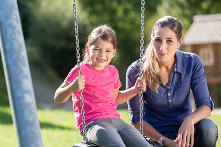 Woman with laughing girl on playground swing having fun togetherの写真素材
