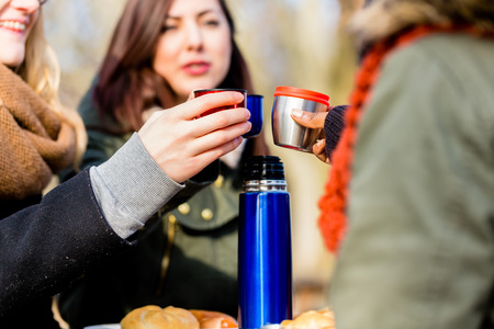 Young female friends talking while drinking a hot beverage outdoors in a winter dayの写真素材