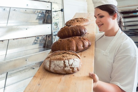Fresh bread on a board in bakehouse of bakery being held by a female baker