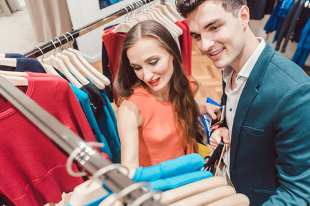 Woman and man shopping fashion in a store, the clothes hanging on a railの写真素材
