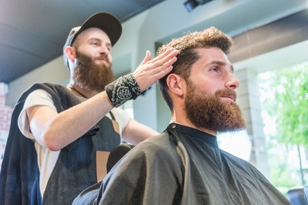 Low-angle view of a handsome bearded young man, ready for a trendy haircut done by an experienced hairstylist in a cool beauty salon for menの写真素材