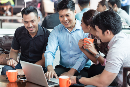 Team of four dedicated employees sitting in front of a laptop while working together at an innovative business project in a modern officeの写真素材