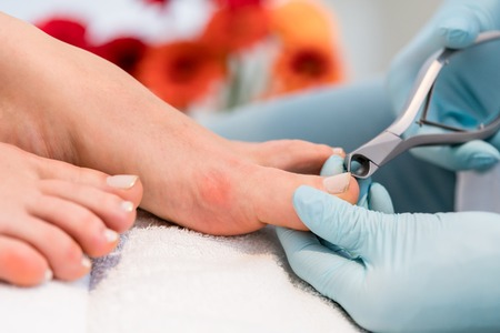 Close-up of the hands of a pedicurist wearing sterile surgical gloves, while using a toe nail clipper while shaping the nails of a female customer in a beauty salonの写真素材