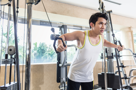 Low-angle view portrait of an Asian handsome man looking down with concentration while exercising cable crossover for chest muscles at the gymの写真素材