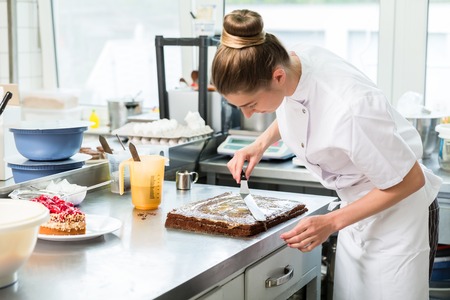Confectioner woman getting chocolate cake ready with topping put onの写真素材
