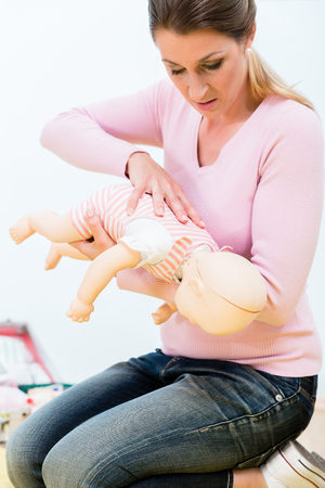 Woman in first aid course practicing revival of infant on baby dollの写真素材