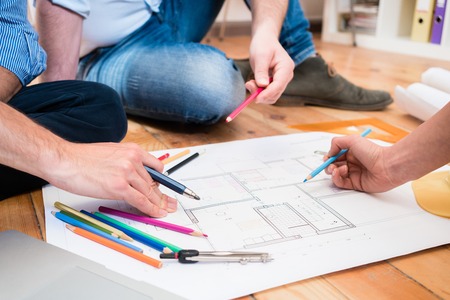 Team of architects and civil engineers sitting on floor with construction plans spreaded