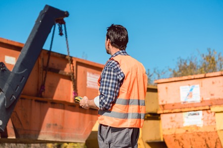 Worker on construction site unloading container for waste from truck using remote control の写真素材