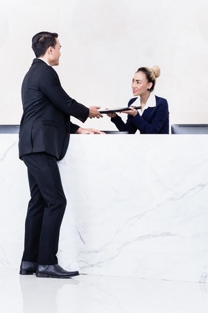 Job Applicant at business front desk giving his documents to receptionistの写真素材