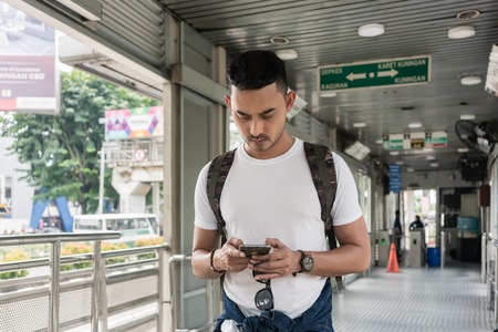 Young man sending messages or browsing the internet on the mobile phone while waiting indoors in a bus station in Jakartaの写真素材
