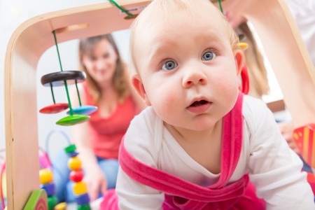 Close-up portrait of a cute baby girl with blue eyes and an intelligent facial expression, while playing on the floor with her mother at homeの写真素材