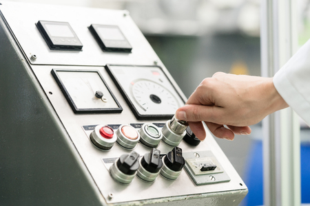 Close-up of the hand of a woman wearing white lab coat, while turning on an industrial machine with...
