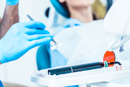 Close-up of the hand of a dentist wearing sterile surgery gloves, while preparing a dental LED curing light machine for treating a patient in a modern clinicの写真素材