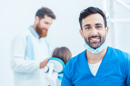 Portrait of a confident dental surgeon wearing blue protective uniform and surgical mask while looking at camera in a modern dental office with reliable specialistsの写真素材