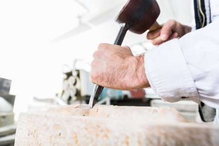 Stonemason cutting boulder with hammer and chisel in workshopの写真素材