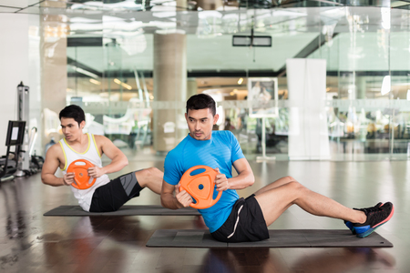 Full length side view of a determined young man holding a weight plate, while exercising Russian twist for core and oblique abdominal muscles at the gymの写真素材