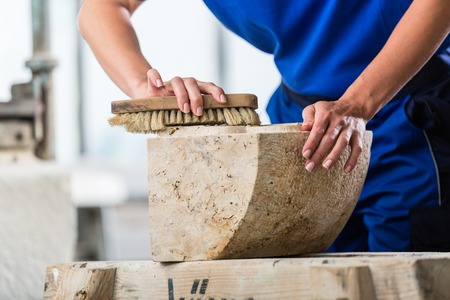 Stonemason brushing stone dust off workpiece in workshopの写真素材