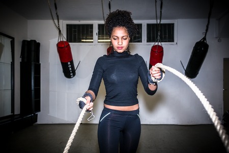 Young fit woman exercising with battle ropes during functional training indoors