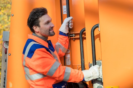 Waste collector gripping handle of garbage truck riding on the platformの写真素材
