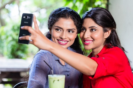 Indian girls in cafe taking selfie with smart phoneの写真素材