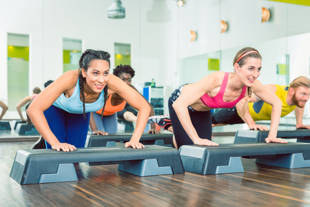 Determined young women exercising push-ups on aerobic stepper platforms during group workout class at a modern fitness clubの写真素材