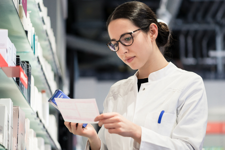 Low-angle portrait of an experienced female pharmacist checking the medical prescription of a pharmaceutical drug, while working in the interior of a modern drugstore with various productsの写真素材