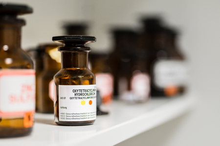 Close-up of the labeled glass container of a chemical pharmaceutical substance on a shelf, next to various supplies in the storage of a modern drugstoreの写真素材