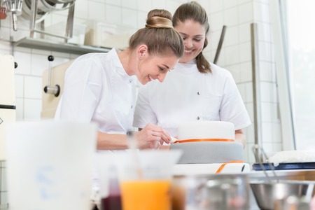 Women in fine bakery or pastry shop baking cakes helping each otherの写真素材