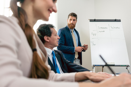 Reliable expert wearing formal business suit while conducting a SWOT analysis during board of directors meeting in the conference room of a successful companyの写真素材