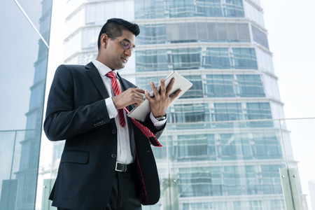 Indian businessman analyzing financial report on a tablet PC indoors at the officeの写真素材