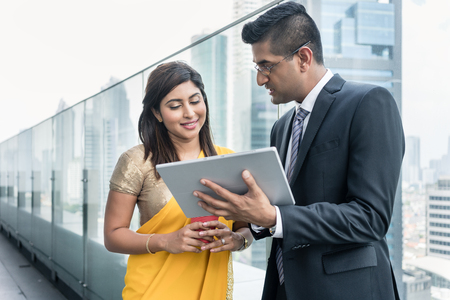Two Indian colleagues analyzing information while using a tablet on the top of a modern building
