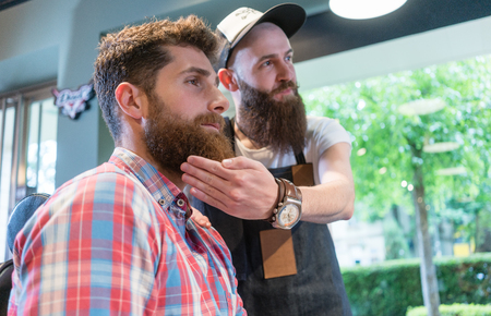 Low-angle view of a bearded young man thinking of a trendy change of look, while looking in the mirror with his experienced hairstylist in the hair salonの写真素材