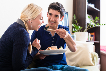 Funny young couple sharing Japanese traditional food during romantic dinner at homeの写真素材