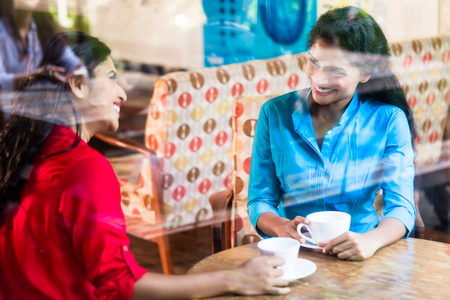 Two Indian woman in cafe, sitting, view through shop windowの写真素材