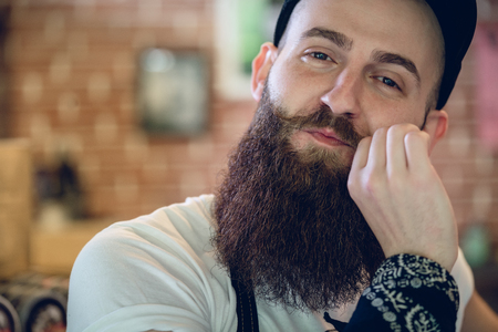 Close-up portrait of a young and fashionable male hairstylist with cool hipster beard and mustache smiling while looking at camera with confidenceの写真素材