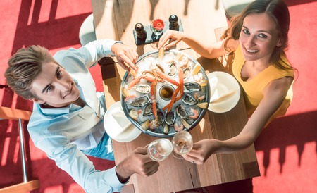 High-angle view of a happy young couple toasting with champagne during romantic dinner with fresh seafood at a trendy restaurantの写真素材