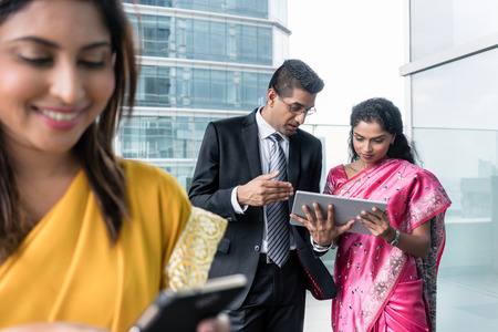 Three Indian business people using modern devices connected to the internet indoorsの写真素材