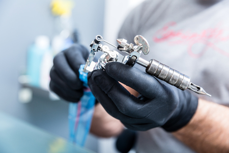 Close-up of the hands of a skilled tattoo artist wearing black gloves while setting a sterile machine for tattooing in a modern studioの写真素材