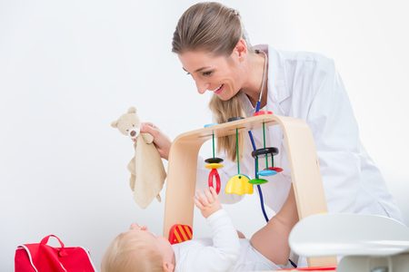 Dedicated female pediatrician smiling while playing with a healthy and active baby during physical exam in a modern medical center for childrenの写真素材