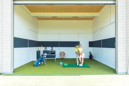 Full length of a dedicated golf coach using modern equipment, while teaching a young woman the correct movement for striking the ball as a professional playerの写真素材