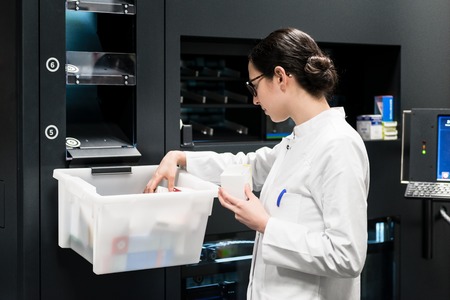 Side view of a dedicated female pharmacist choosing the best medicines from a plastic box during work in a contemporary drugstore with modern equipmentの写真素材