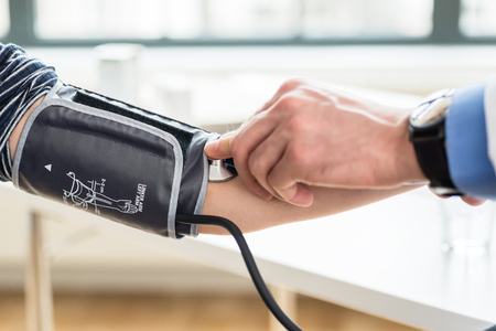 Side view close-up of the hand of a doctor measuring the blood pressure of a patient with a manual instrument during routine check-upの写真素材