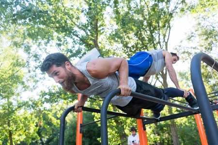 Low-angle view of a strong young man supporting his friend on his back, while doing extreme pull-ups...