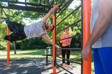 Strong and happy young man gripping a vertical bar while practicing human flag exercise with bent...