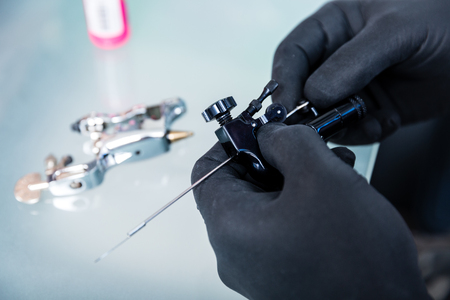 Close-up of the hands of tattoo artist wearing sterile black gloves while preparing the machine for tattooing in a modern studioの写真素材