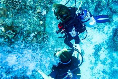 Tourists scuba diving at coral reef under water in tropical ocean